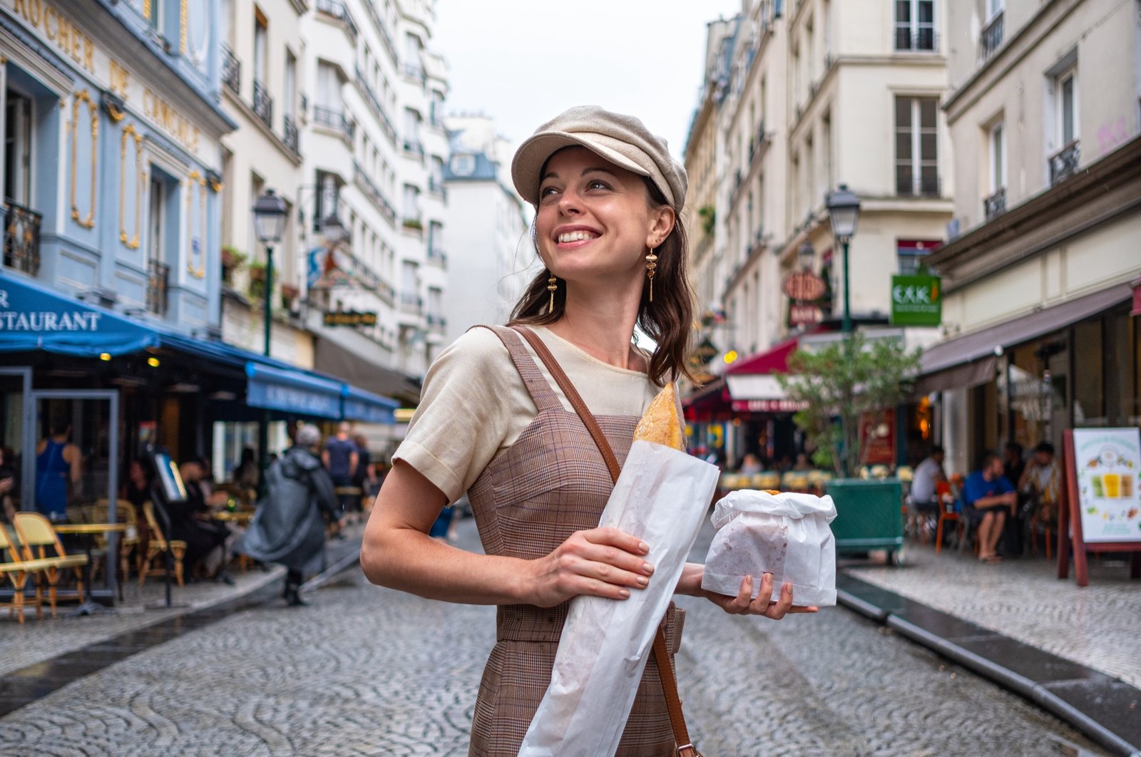A smiling woman holding a baguette on a Parisian street
